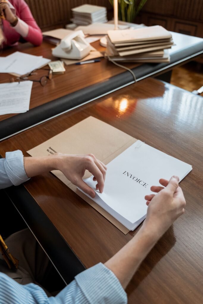 Manos organizando facturas en papel sobre una mesa de trabajo.