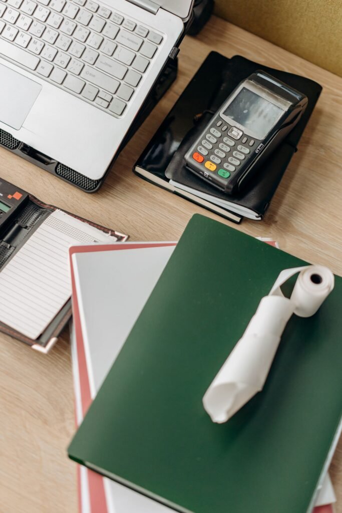 Escritorio con un portátil, un terminal de pago y cuadernos.