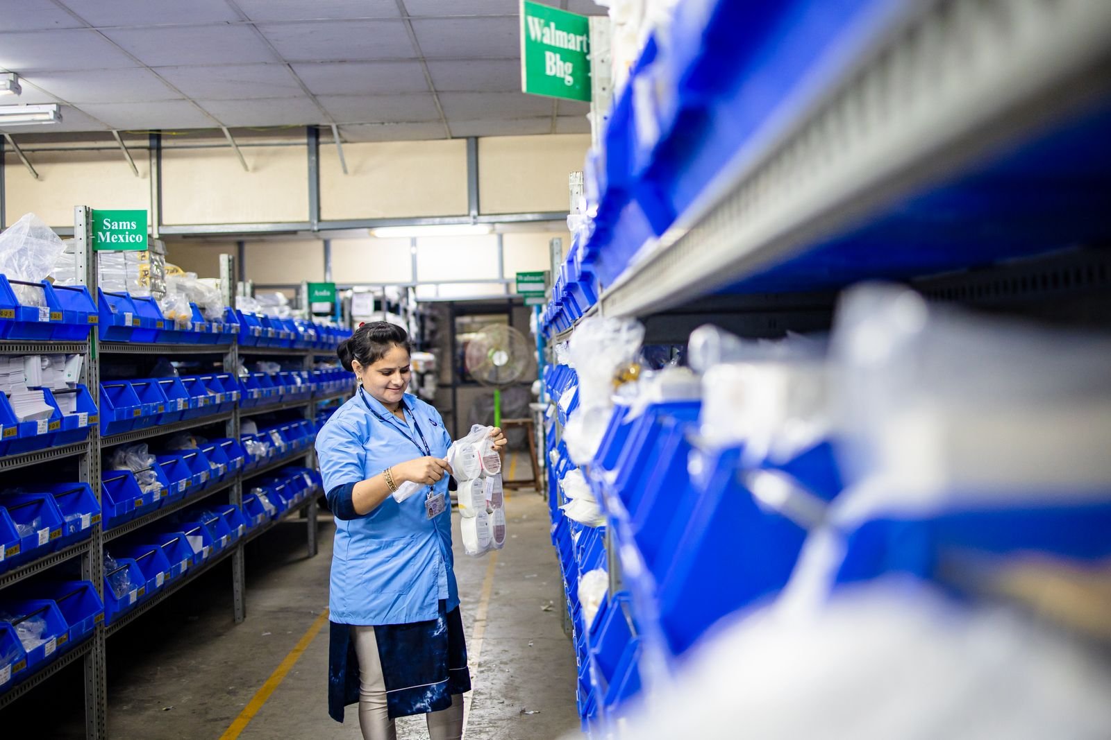 Trabajadora colocando contenedores etiquetados en las estanterías de un almacén.